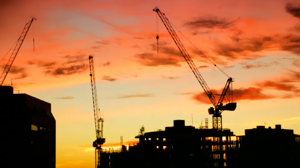 Construction cranes against a sunset sky