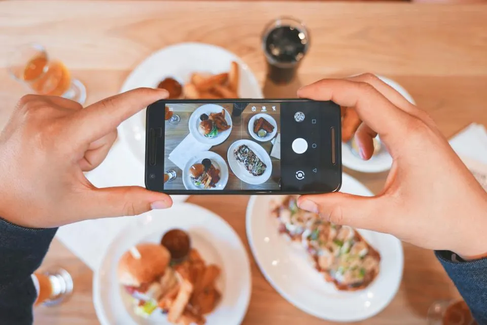 Phone photographing plates of food on a restaurant table