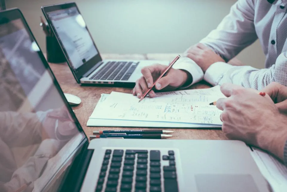 Hands reviewing documents next to a laptop